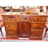 A VICTORIAN MAHOGANY KNEE HOLE DESK WITH SEVEN DRAWERS FLANKING A CENTRAL CABINET ON PLINTH BASE.