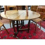 AN ANTIQUE OAK OVAL DROP FLAP TABLE OPENING ON DOUBLE GATE, THE GUN BARREL COLUMNS TO EACH END ON