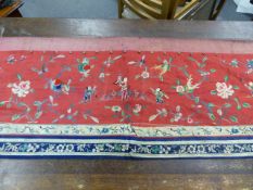 A CHINESE RED SILK FRONTAL EMBROIDERED WITH FOUR CHILDREN HOLDING AUSPICIOUS OBJECTS AMONGST FLOWERS