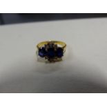 AN 18K STAMPED SAPPHIRE AND DIAMOND RING, THE THREE OVAL CUT SAPPHIRES SURROUNDED IN THE CENTRE BY