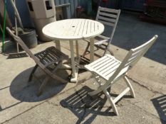 A CIRCULAR TEAK PATIO TABLE WITH THREE SIMILAR FOLDING CHAIRS.