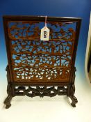 A CHINESE HARDWOOD TABLE SCREEN, THREE OF THE FOUR PANELS WITHIN THE COMMON FRAME PIERCED AND CARVED