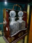 A MAHOGANY TWO BOTTLE TANTALUS, THE BRASS HANDLE AT THE TOP RELEASED BY A BUTTON AND KEY