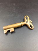 A CARL AUBOCK BRASS BOTTLE OPENER IN THE FORM OF A KEY, THE BARREL WITH CROWN TOP OPENER FLANGE