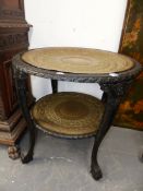 AN EASTERN CARVED EBONY TWO TIER STAND WITH BRASS TRAYS. Dia.70 x H.69cms.