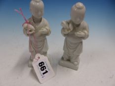 A PAIR OF BLANC DE CHINE FIGURES OF CHILDREN STANDING HOLDING FRUITS. H 12cms.