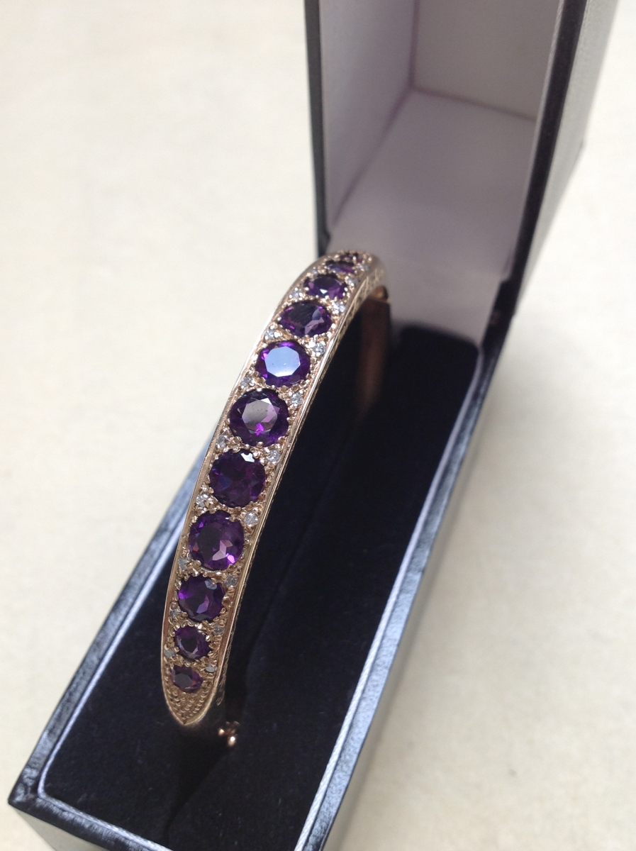 A 9ct GOLD AMETHYST AND DIAMOND CARVED HINGED BANGLE COMPLETE WITH FIGURE OF EIGHT SAFETY CLASP,