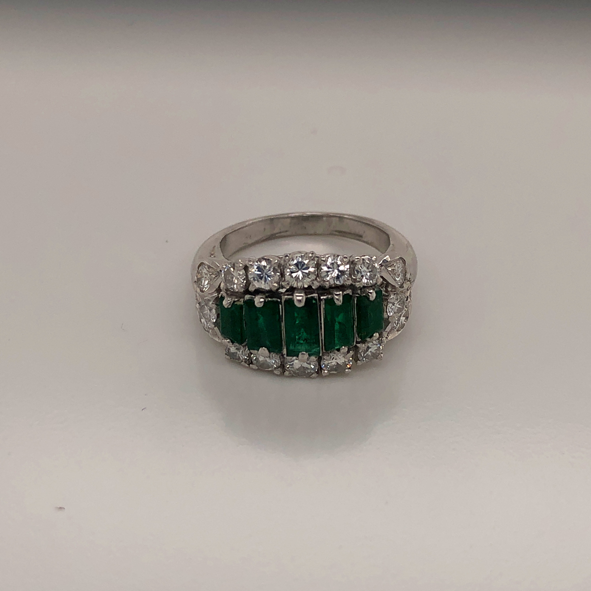 AN EMERALD AND DIAMOND DRESS RING DESIGNED AS A GRADUATED RECTANGLE -SHAPE EMERALD LINE A WITH