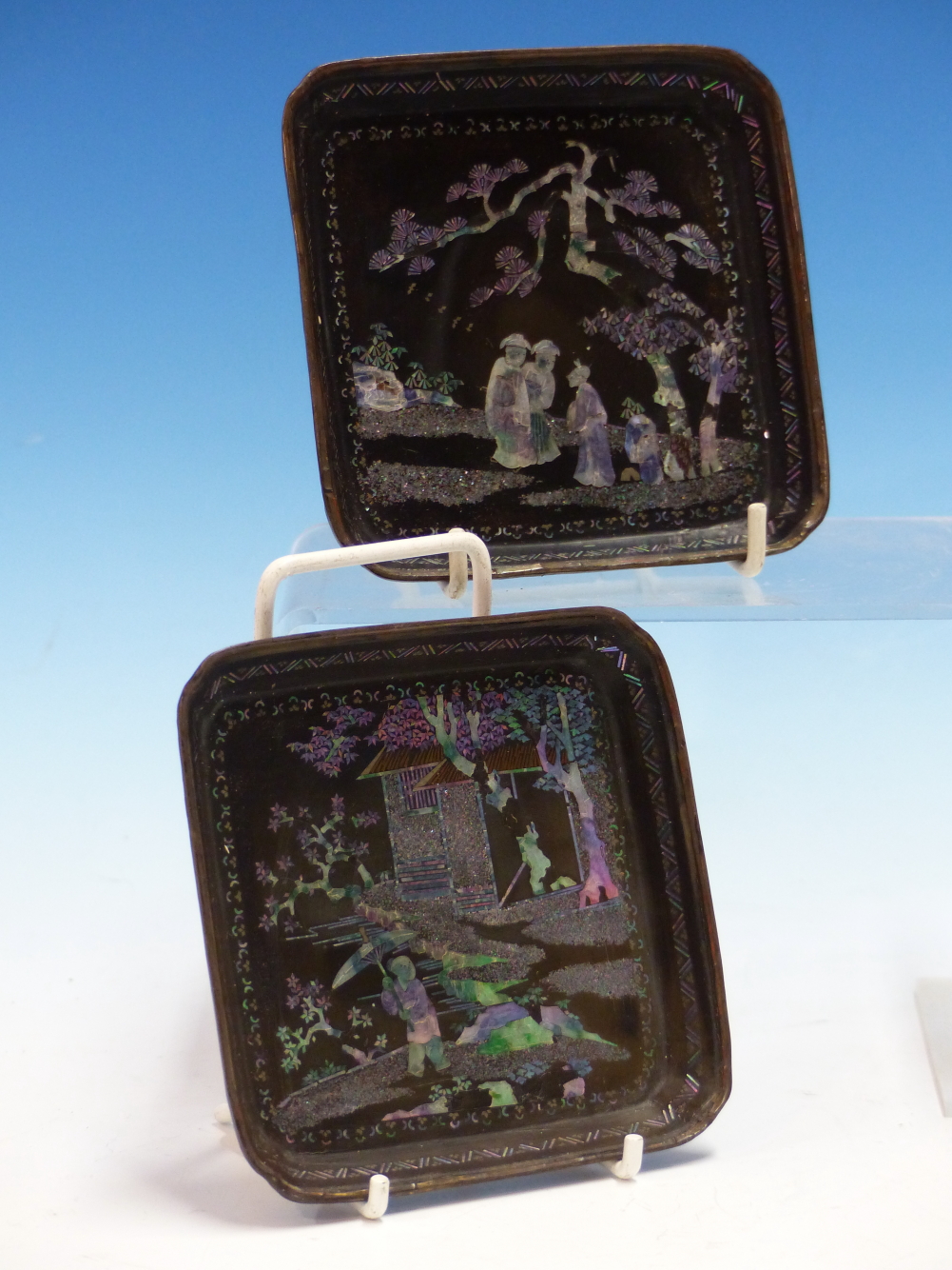 A PAIR OF LAC BURGAUTE SQUARE TRAYS, THE METAL MOUNTED RINGS ENCLOSING MOTHER OF PEARL FIGURES IN