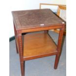 AN ARTS AND CRAFTS MAHOGANY TWO TIER TABLE, THE TOP CARVED IN LOW RELIEF WITH FLOWERS WITHIN CHEVRON