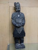 A CHINESE BLACKENED TERRACOTTA SOLDIER STANING WITH HIS HANDS CLASPED ON HIS LACQUER ARMOURED