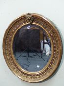 A BEVELLED GLASS OVAL MIRROR IN GILT WOOD FRAME. THE OUTER FOLIAGE BAND ENCLOSING A BLACK GROUND