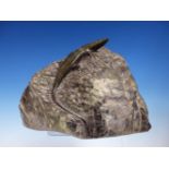 A SERPENTINITE CARVING OF A LIZARD, IT'S BODY POLISHED AGAINST THE ROUGH HEWN ROCK BOULDER,