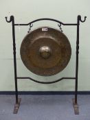 A BELL METAL GONG ON A WROUGHT IRON STAND, THE HOOK TOPPED UPRIGHTS JOINED BY TWO SERPENTINE