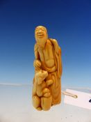 AN IVORY NETSUKE CARVED AS A BEARDED MAN STANDING WITH HIS RIGHT HAND GOING TO PAT THE HEAD OF HIS