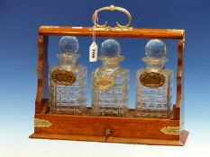 AN OAK THREE BOTTLE TANTALUS, EACH DECANTER WITH ITS LABEL, BRANDY, SHERRY AND SCOTCH.