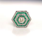 A WHITE METAL, EMERALD AND DIAMOND GEOMETRIC GRAIN SET CLUSTER RING. THE CENTRAL DIAMOND