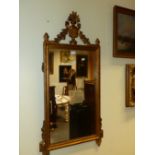 A RECTANGULAR MIRROR IN A GILT FRAME CRESTED BY A VASE OF FLOWERS AND SWAGS, THE BASE WITH