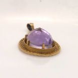 A YELLOW METAL OPEN WORK PENDANT REVERSE SET WITH AN OVAL FACETED PURPLE GEMSTONE. DROP 5.5cms,