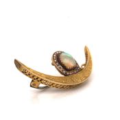 AN INDIAN FOLIATE ENGRAVED YELLOW METAL CRESCENT BROOCH, SURMOUNTED BY A D-SHAPED OPAL WITHIN A