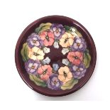 Moorcroft plate, with a tube lined floral design on a puce ground, factory stamp to base, 26cms diam