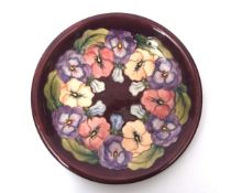 Moorcroft plate, with a tube lined floral design on a puce ground, factory stamp to base, 26cms diam