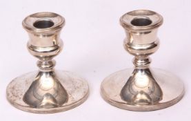 Two Elizabeth II squat candlesticks with fixed urn shaped sconces on spreading circular bases (