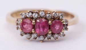 Precious metal ruby and diamond cluster ring, the 3 graduated rubies claw set and raised within a