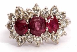 Precious metal ruby and diamond cluster ring, features three graduated oval cut rubies, surrounded