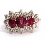 Precious metal ruby and diamond cluster ring, features three graduated oval cut rubies, surrounded