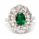 18ct white gold, emerald and diamond cluster ring, the oval shaped faceted emerald raised within a