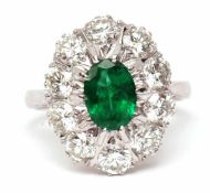 18ct white gold, emerald and diamond cluster ring, the oval shaped faceted emerald raised within a