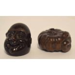 Two carved netsuke, one modelled as a snake coiled within a shell, the other with the face of Buddha