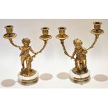 Two gilt metal and white composite two-light candelabra, each modelled in the form of male and