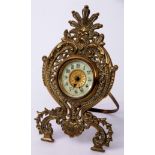 Late 19th/early 20th century cast brass easel backed timepiece, the pierced and shaped foliate