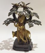 Bronze model of Krishna standing below foliage with peacocks in branches with cow in background,