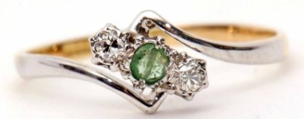 Modern precious metal and diamond and emerald cross-over ring, the pale small emerald set between