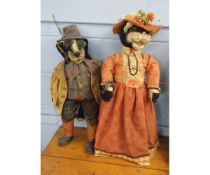 Two large plush display characters depicting a badger and a cat, both clothed, the larger