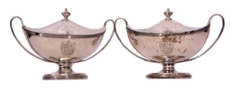 Two George III lidded tureens each of oval form with tapering strapwork handles and raised on