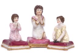 Group of three mid-19th century porcelain models of children kneeling on cushions at prayer by Derby