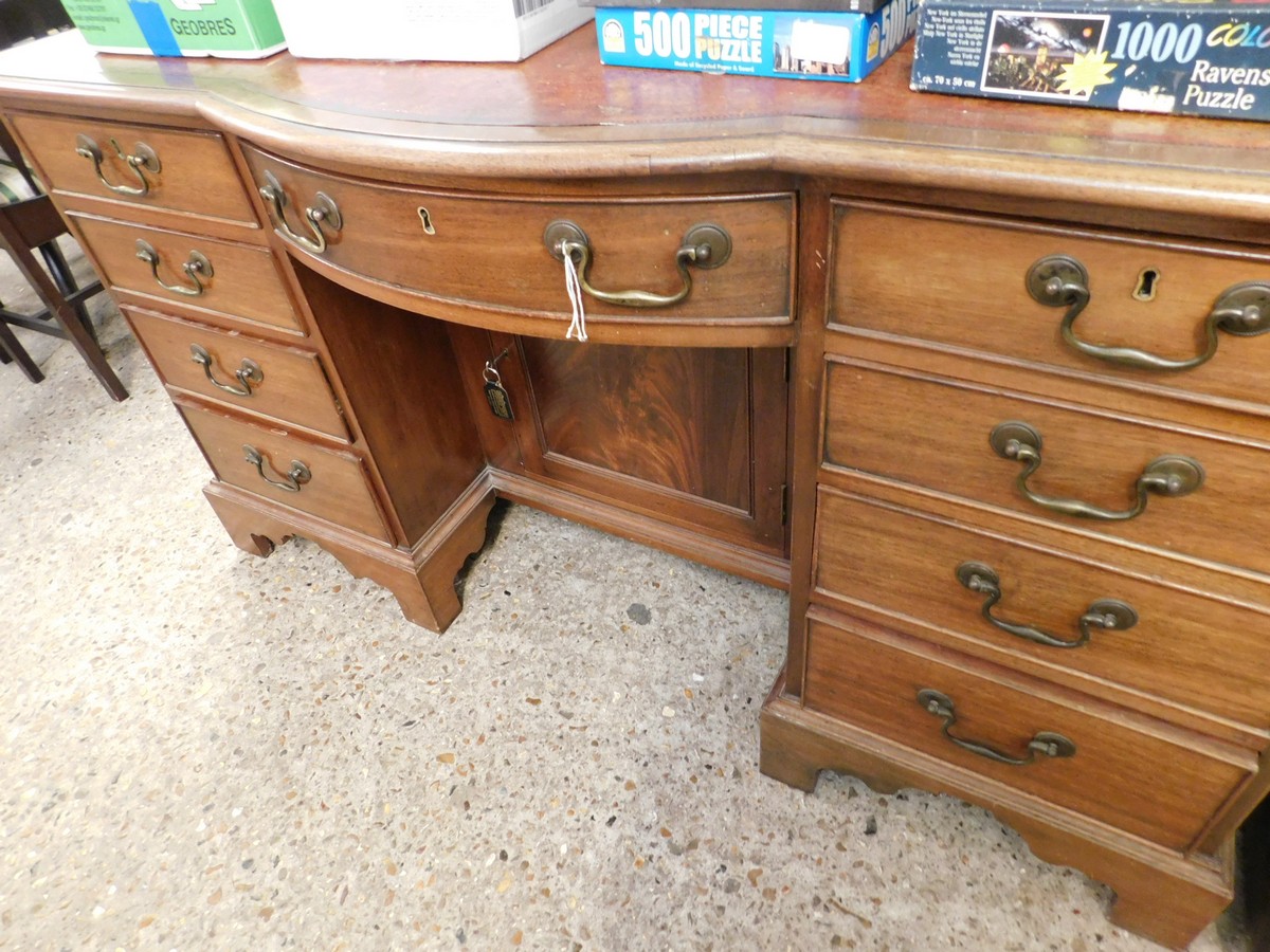 MAHOGANY FRAMED BOW FRONTED LEATHER TOPPED DESK WITH NINE DRAWERS AND ONE CUPBOARD DOOR WITH RED