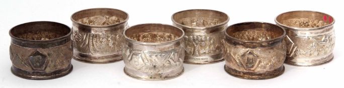Six white metal cylindrical napkin rings, each embossed with elephants, trees and mountains with