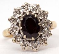 18ct gold garnet and diamond cluster ring, the oval shaped faceted garnet claw set and raised within