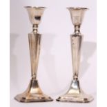 Two George V single candlesticks, each with fixed and faceted square sconces on tapering columns and