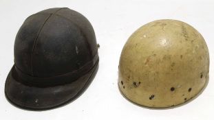 Two vintage motorcycle helmets: one black leather covered with peak, the other cream coloured