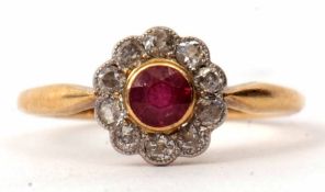 An 18ct ruby and diamond cluster ring, the circular cut faceted ruby bezel set in a surround of