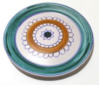 Large Poole type charger with a circular and looped design to the centre within a green wash border,