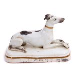 Mid-19th century English porcelain model of a greyhound with black markings seated on a shaped white