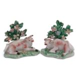 Two 18th century Derby models of bulls seated on green shaped bases with leafy bocage behind, 7cm