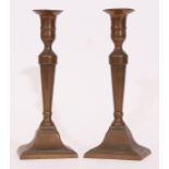 Pair of bronze or cast metal candlesticks, moulded stems and spreading square bases, the bases